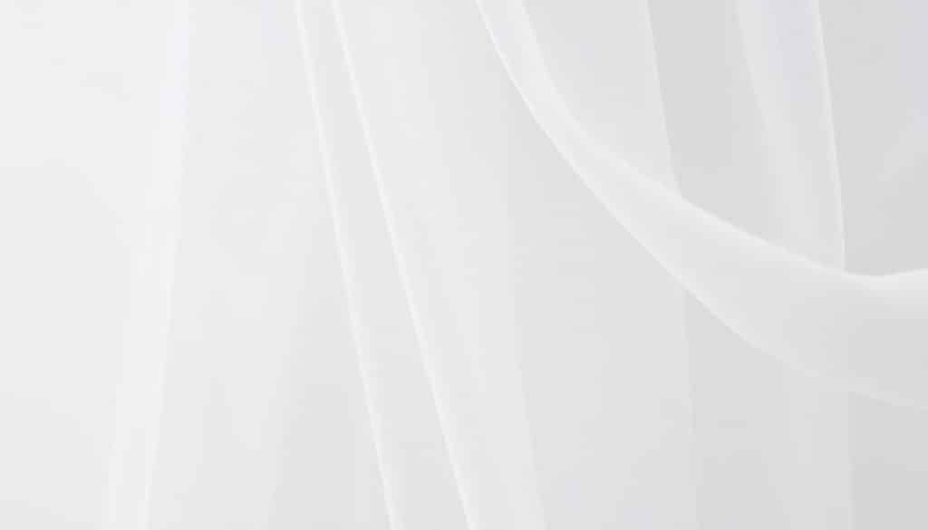 A delicate tulle fabric in a soft, airy texture fills the frame, draped elegantly against a clean, minimalist background. The tulle's sheer, diaphanous nature is captured in fine detail, with subtle folds and ripples that suggest the gentle movement of the material. Soft, diffused lighting bathes the scene, creating a serene, ethereal atmosphere that emphasizes the fragile, gossamer-like quality of the tulle. The camera angle is positioned to highlight the intricate stitching and delicate craftsmanship required to work with this delicate textile, offering a close-up, textural view that invites the viewer to appreciate the technical mastery behind creating beautiful tulle garments. Overall, the image conveys a sense of elegant simplicity, showcasing the versatility and beauty of tulle sewing techniques.